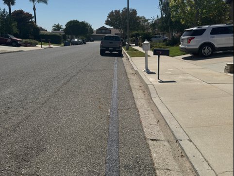 The same cut sealed flush with the road surface, a clean line along the gutter with no patchwork around it