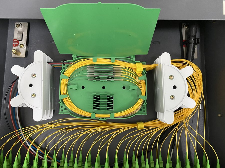 A splice tray open in a cabinet, yellow pigtails dressed into rows of green connectors