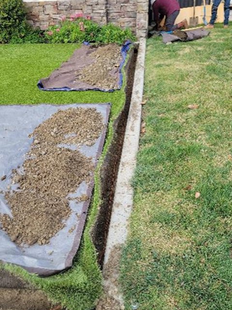 A narrow drop bury open along a front lawn, the turf lifted in strips onto protection mats with the spoil kept off the grass